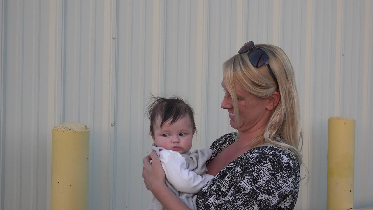 Woman holding baby beside yellow bollards and metal wall