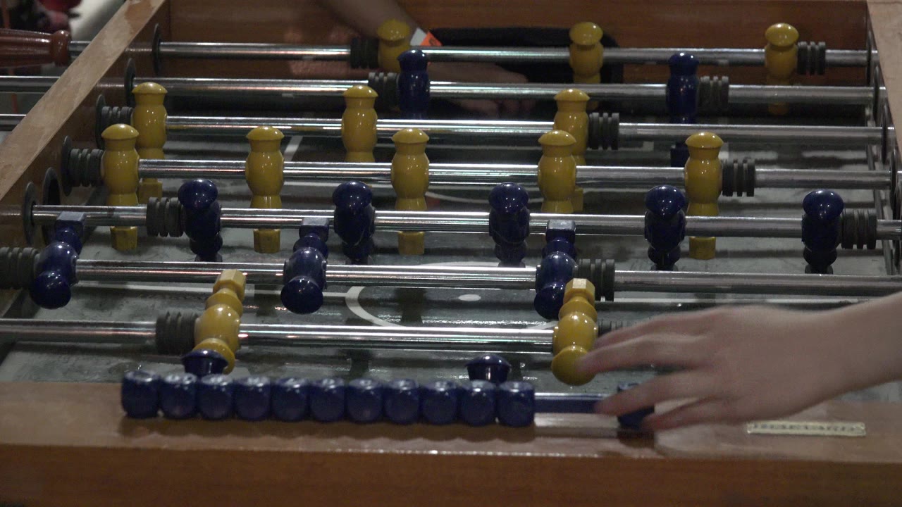 Foosball table with blue and yellow figures and a hand near the lower edge.
