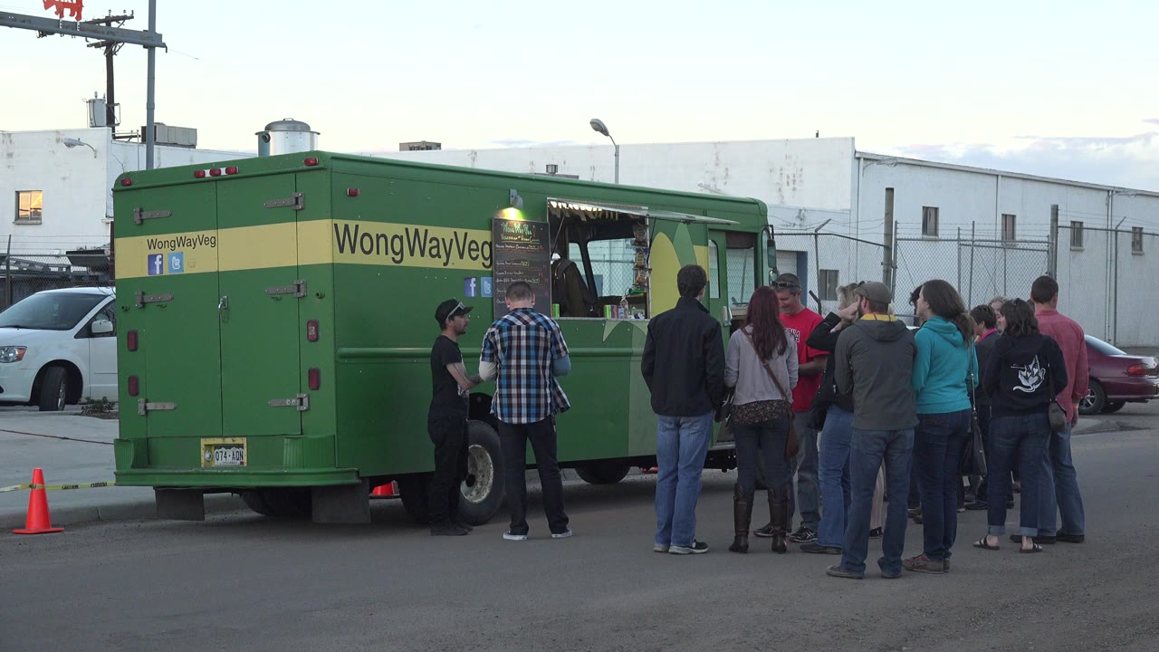 People standing in line beside a green food truck on a street.