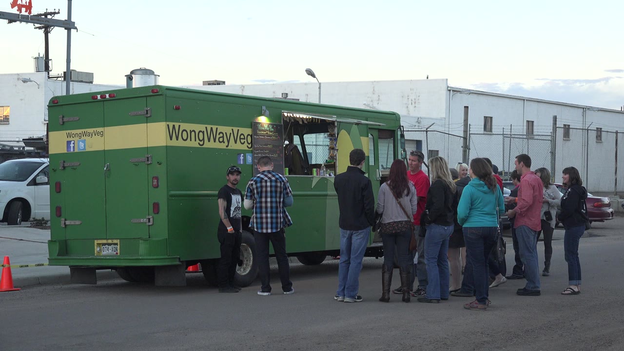 Adults waiting beside a green food truck in a parking lot.