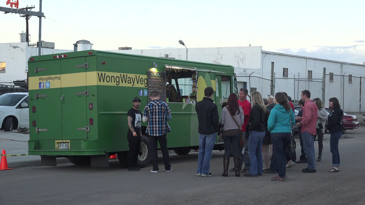 At 0:01, the Denver food truck line remains centered, with several adults facing the service window and a traffic cone near the truck's rear.