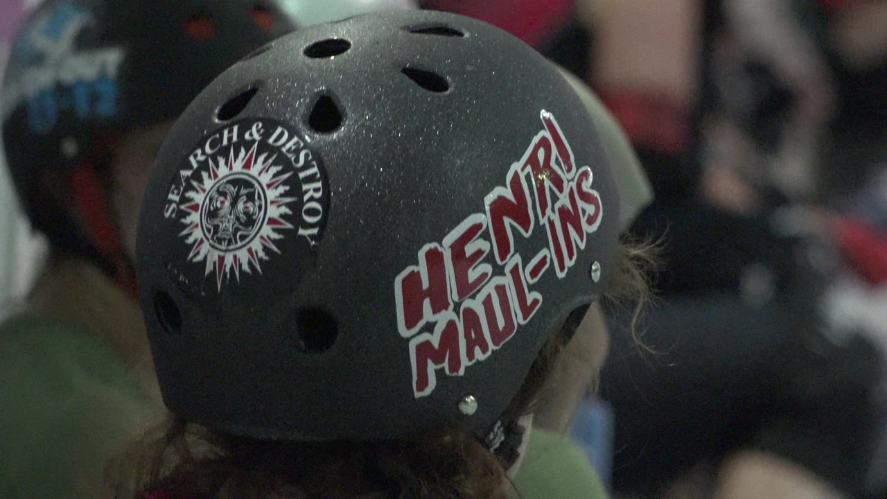 A black helmet with large red and white lettering and a round sticker stays centered, with nearby helmeted people softly out of focus in Denver, Colorado.