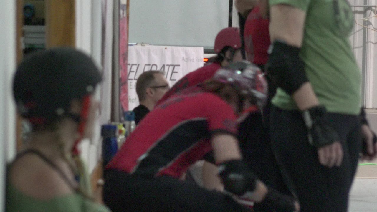 Helmeted skaters seated and standing near an indoor bench