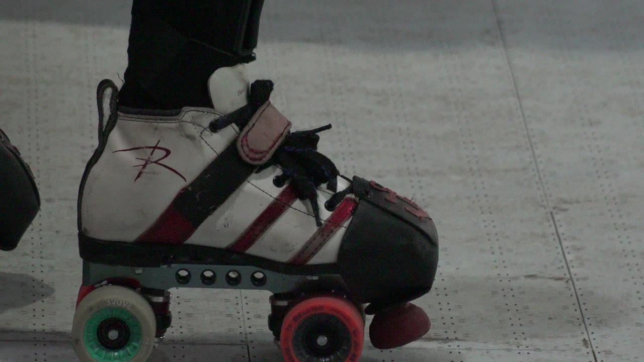 At 0:00, a white roller skate with black toe guard, red striping, mixed-color wheels, and black pants above the boot fills the frame in Denver, with no visible faces.