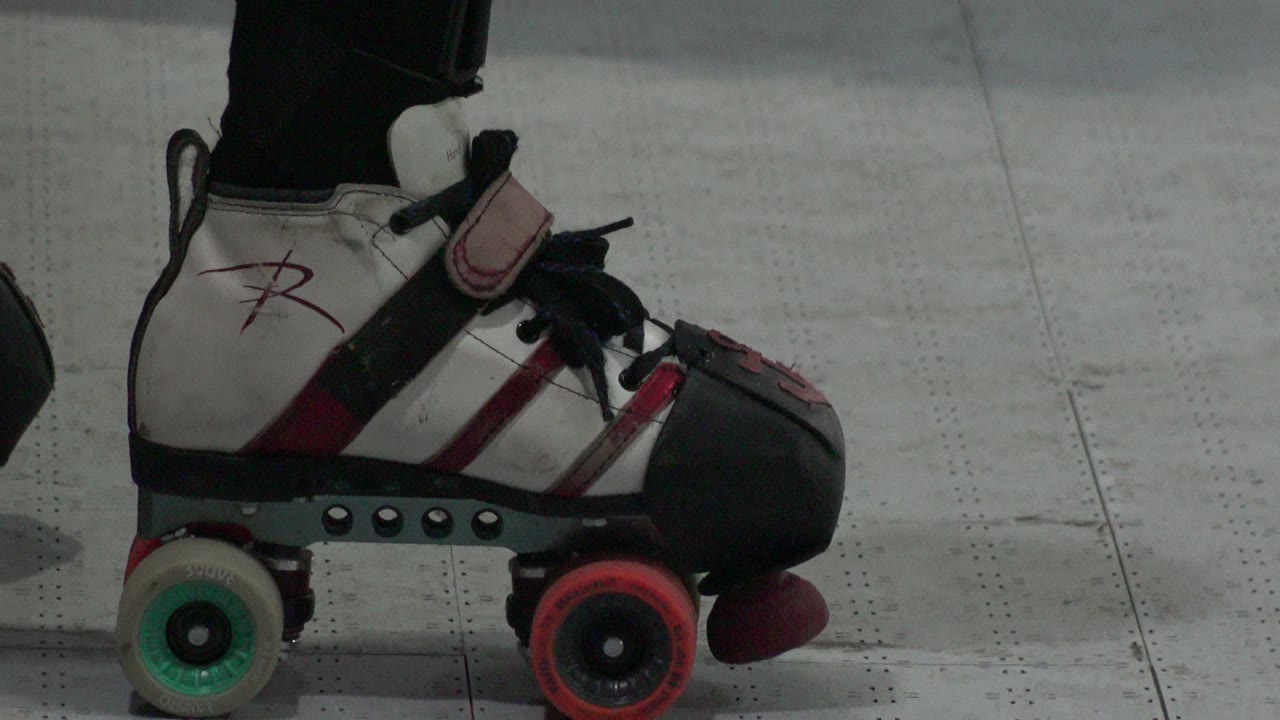 Roller skate close-up with the toe pointed right and wheels aligned over a floor seam.
