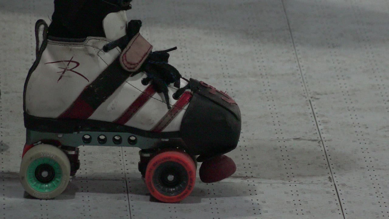 Close side view of a white, black, and red quad roller skate in Denver, Colorado, with green and red wheels on a gray indoor floor.