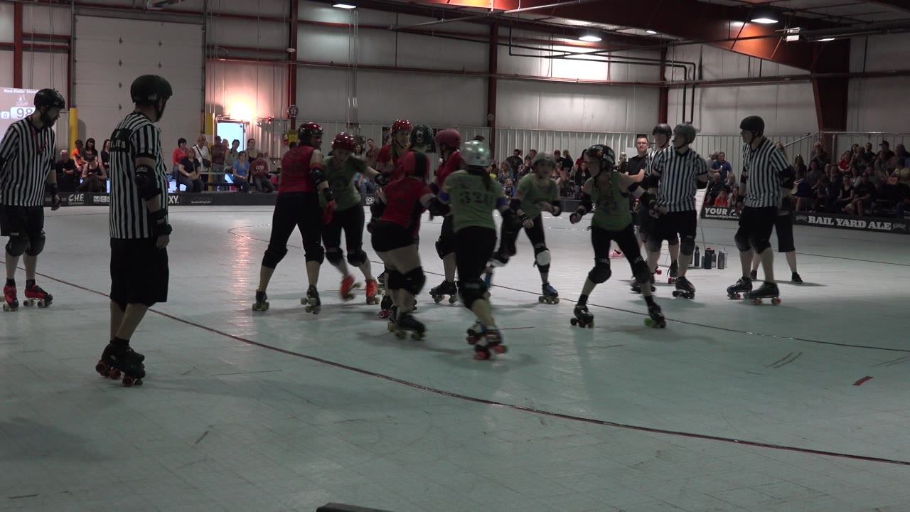 In Denver, Colorado, a pack of green- and red-shirted roller skaters bunches near the center of the rink with referees positioned around them.