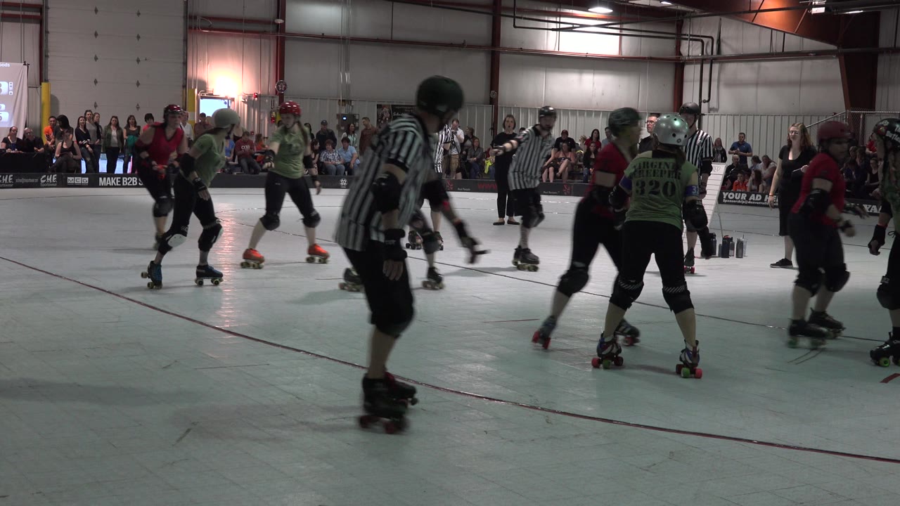 A referee skates across the foreground as derby players continue behind him.