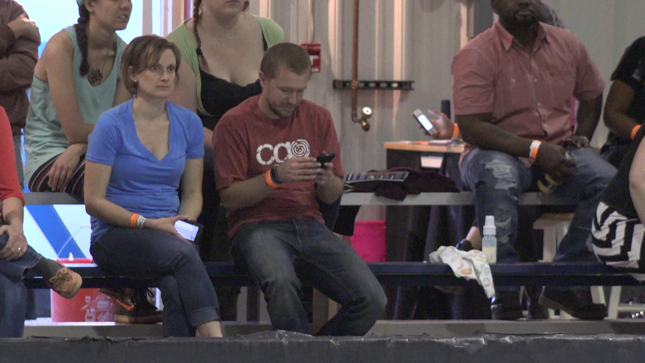Spectators sit behind a blurred referee at an indoor roller derby event.