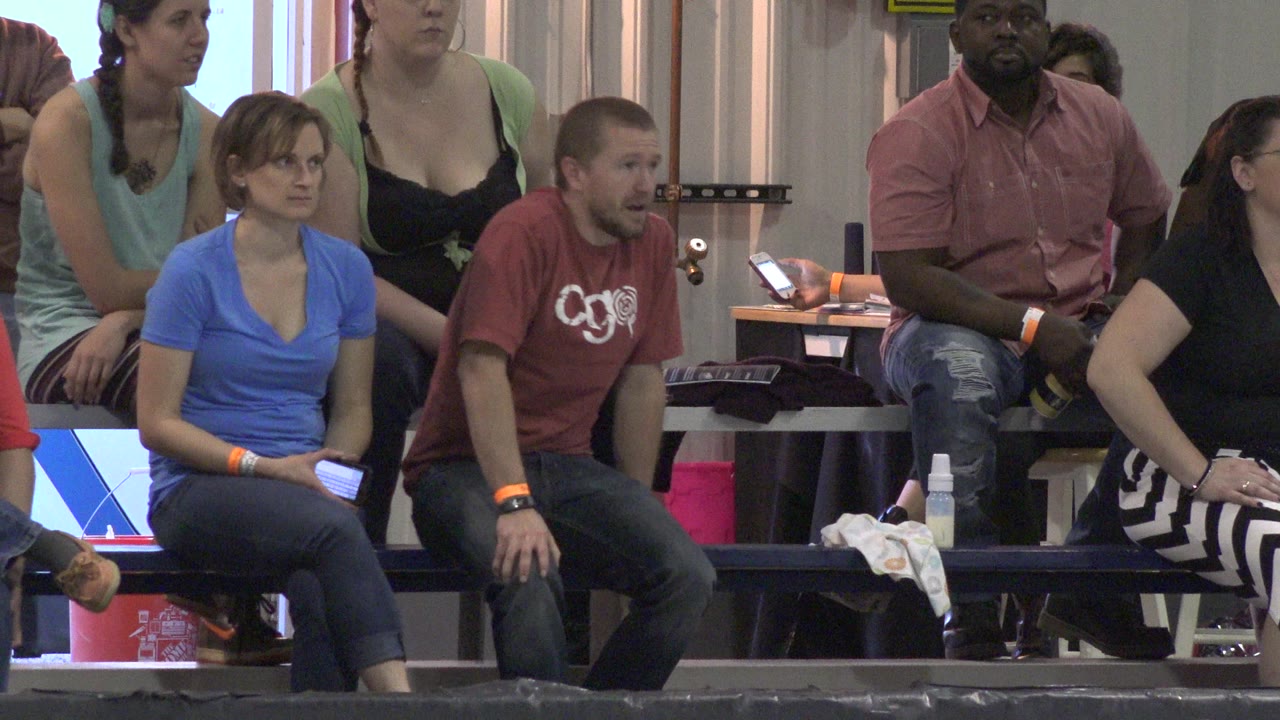 The Denver indoor stands remain filled by seated adults, with a phone glowing at the back and personal bags on the bench beside the group.