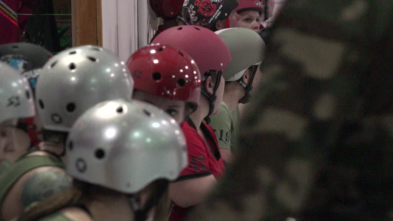 Helmeted people crowded indoors behind a dark foreground obstruction.
