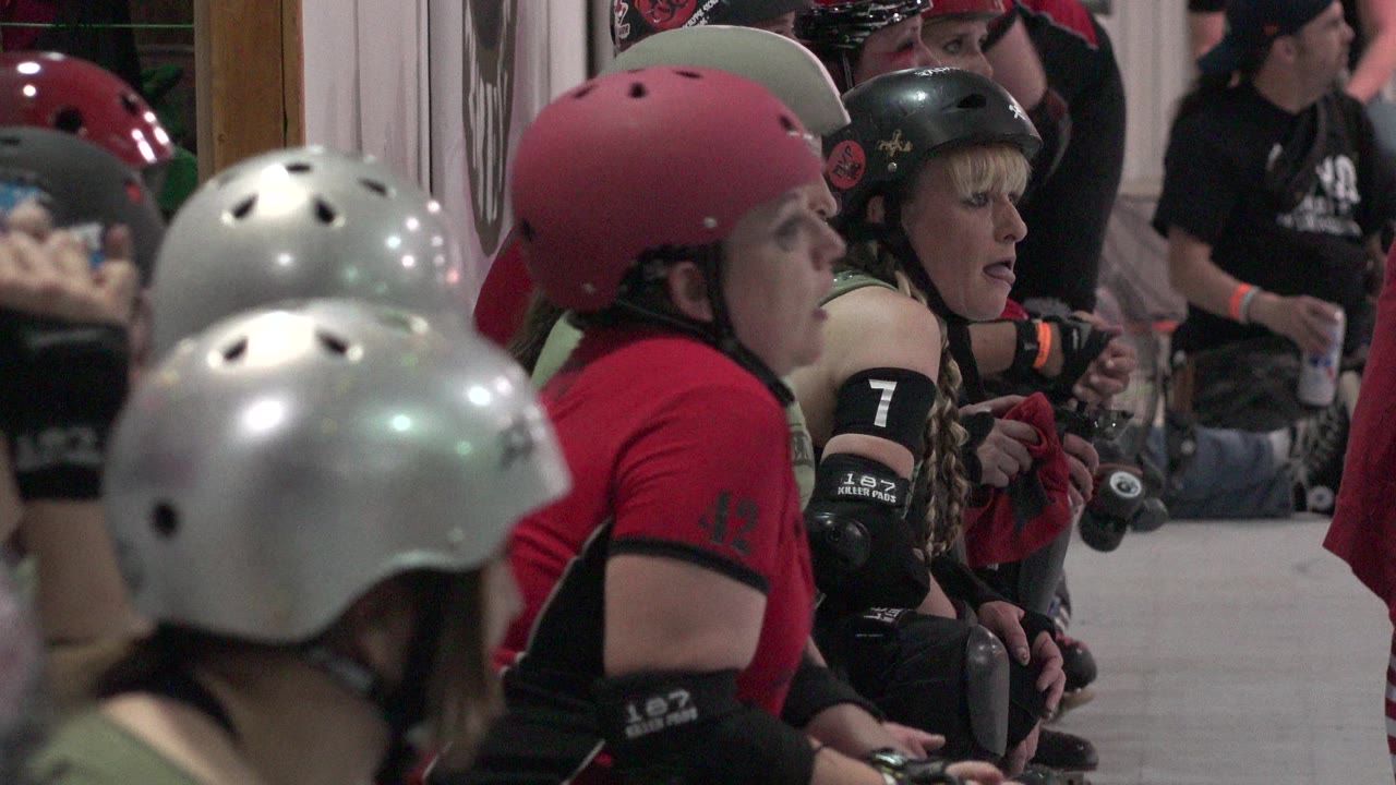 Helmeted roller derby players seated beside an indoor rink.