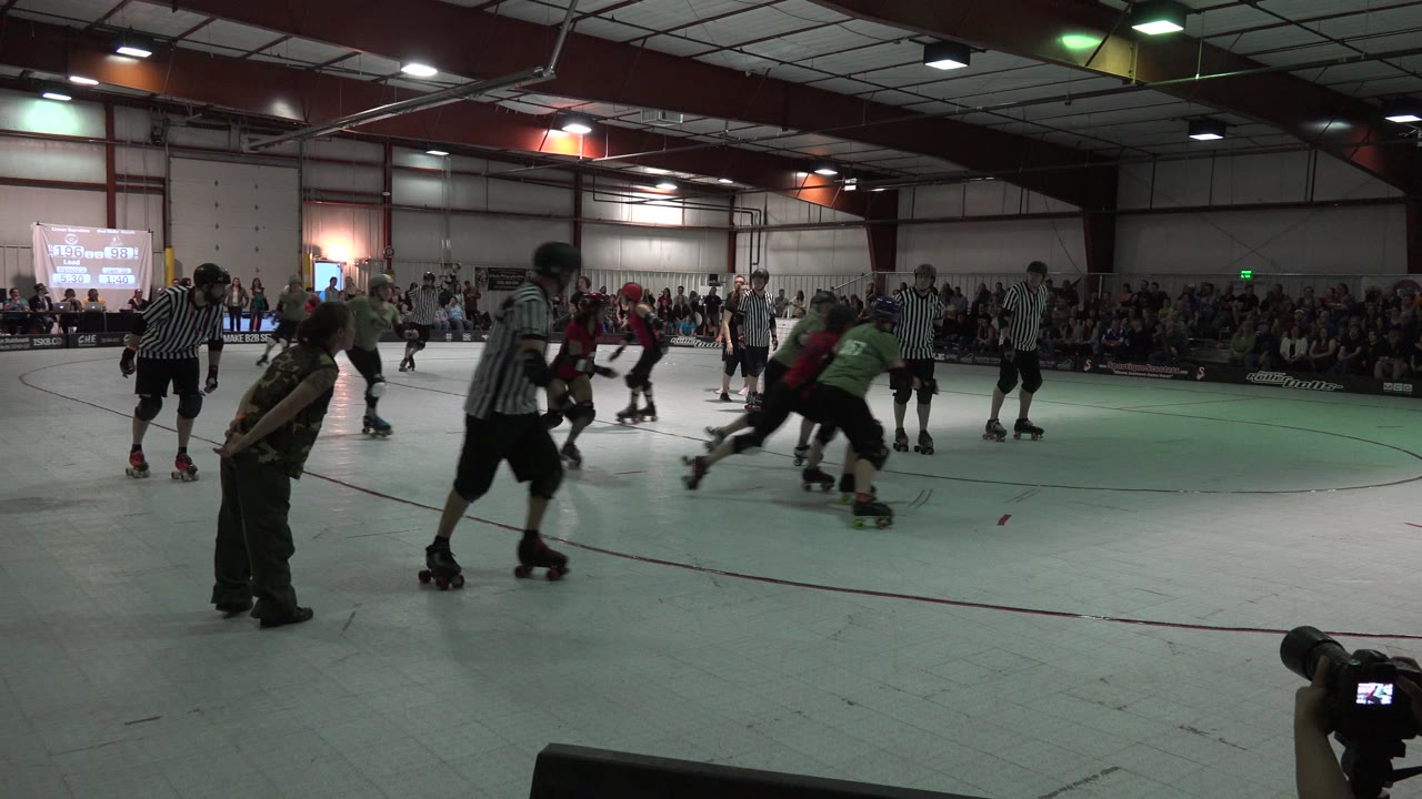 In Denver, Colorado, roller derby skaters move across an indoor rink while striped referees and a seated crowd fill the background.