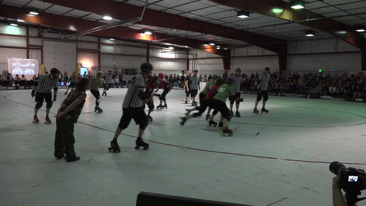 In Denver, Colorado, helmeted roller derby skaters cluster near striped officials as spectators watch from the far side of the indoor rink.