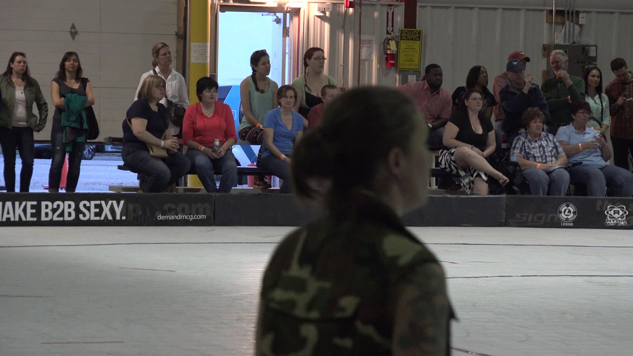 Spectators sit and stand behind rink boards while a blurred figure crosses the foreground.