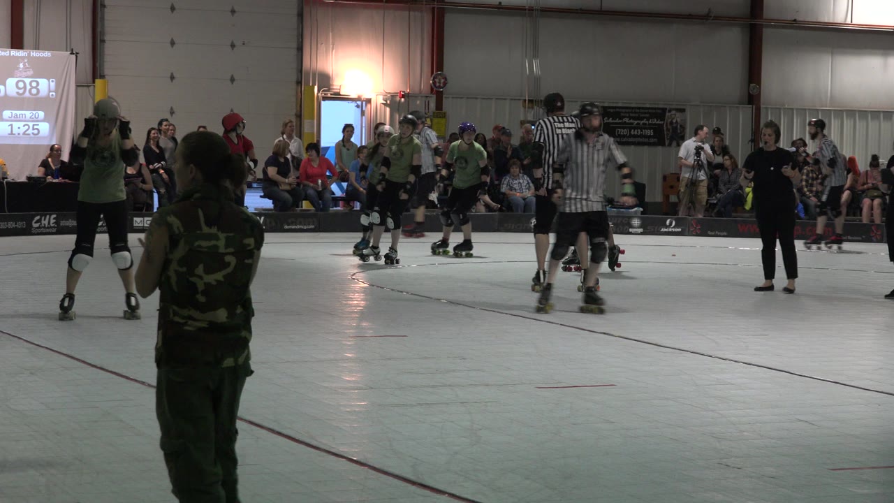 Roller skaters and referees on an indoor rink with spectators behind them.