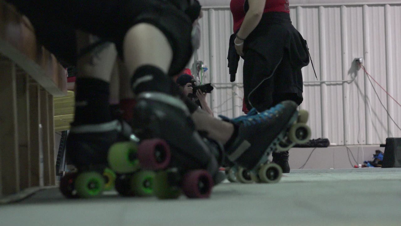 Low-angle view of roller skates and legs near an indoor floor.