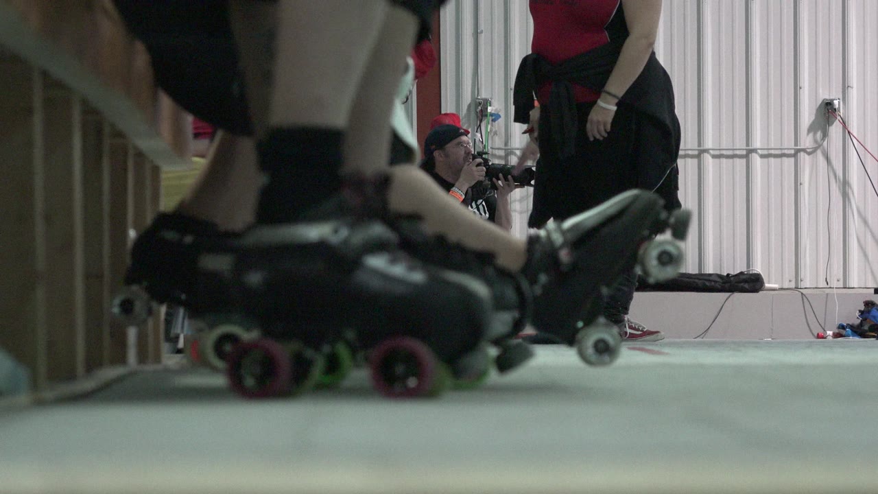 Close-up of black roller skates beside a wooden barrier.