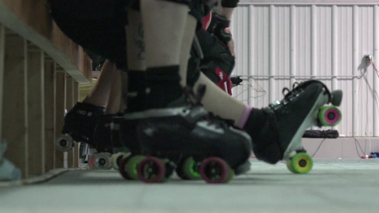 Floor-level Denver frame showing multiple black roller skates close together, with pink and green wheels in front and a pale windowed wall in the background.