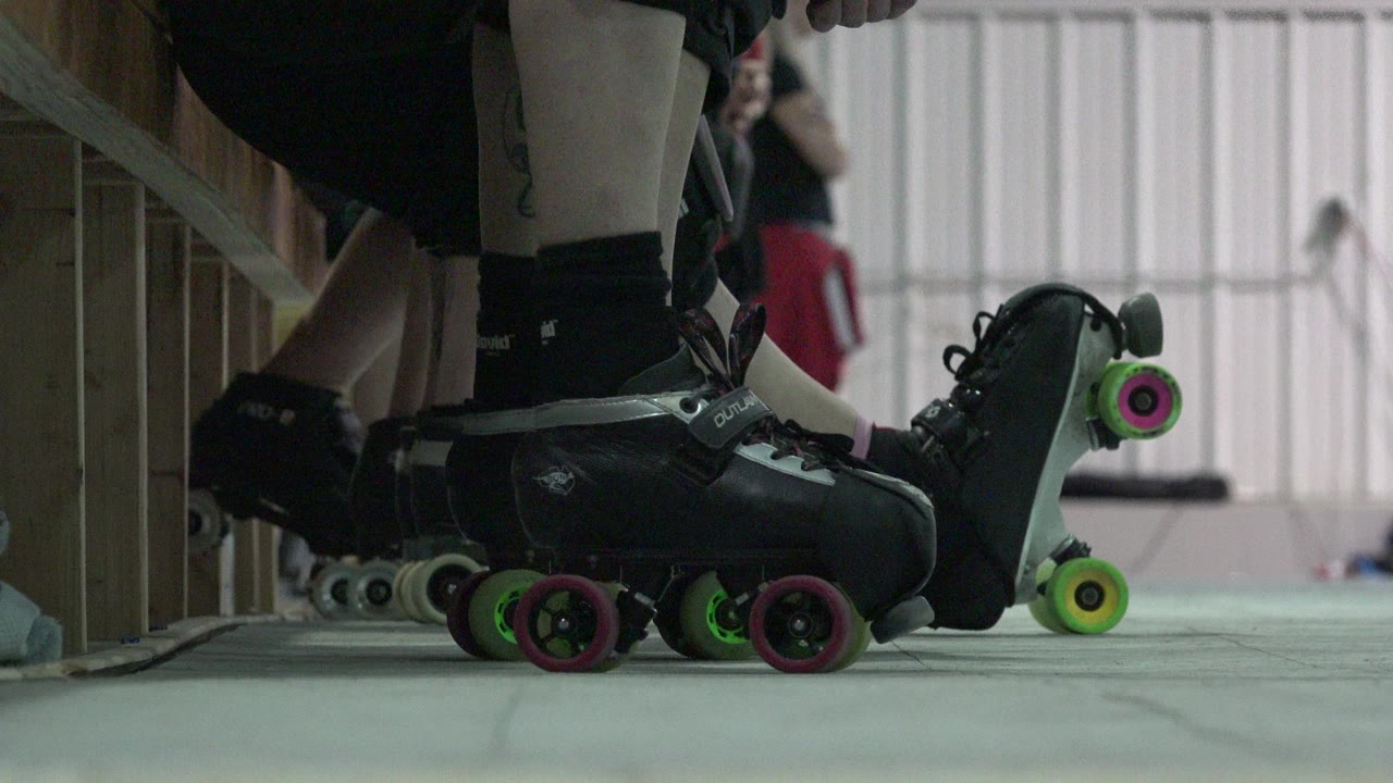 A Denver indoor waiting moment shows foreground roller skates pressed close together, with pink and green wheels visible and background figures out of focus.