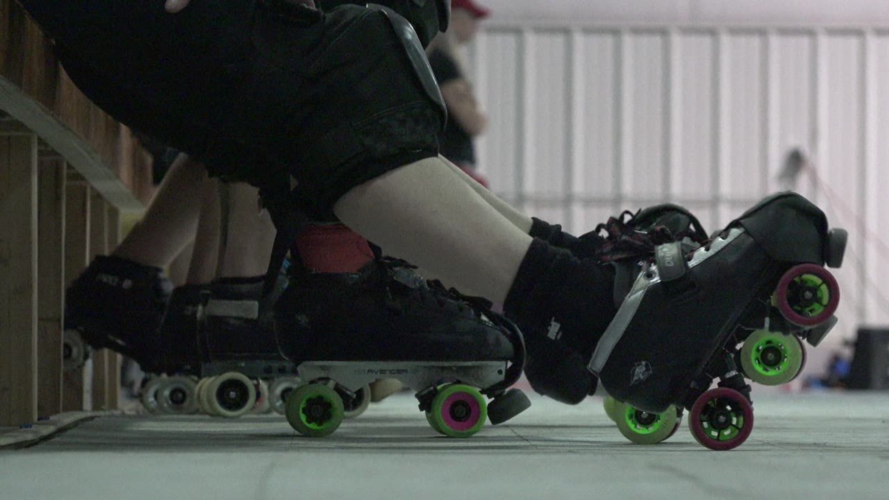 Ground-level Denver 2015 view of multiple quad skates clustered under and beside the bench, with bright wheels and lower legs filling the foreground.