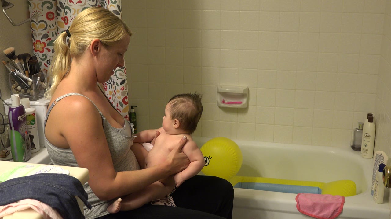 Mother holding a young child beside a bathtub.