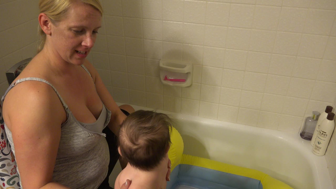 Mother stands beside a baby at a bathtub with an inflatable toy.