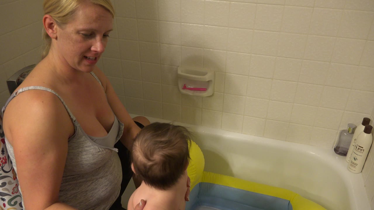 In Westminster, Colorado, the mother looks down toward the baby as the child sits or stands near the inflatable toy inside the bathtub area.