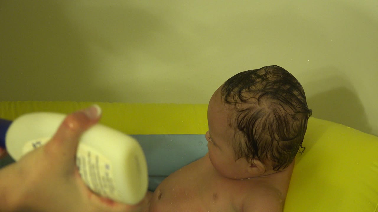 Adult hand holds soap near a baby in bathwater.