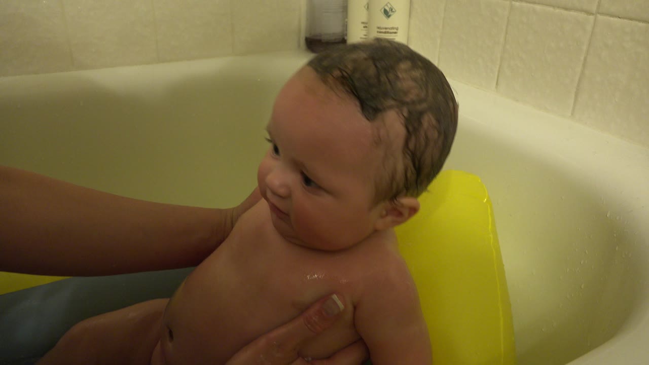 Infant turns toward the side of a bathtub with caregiver support.