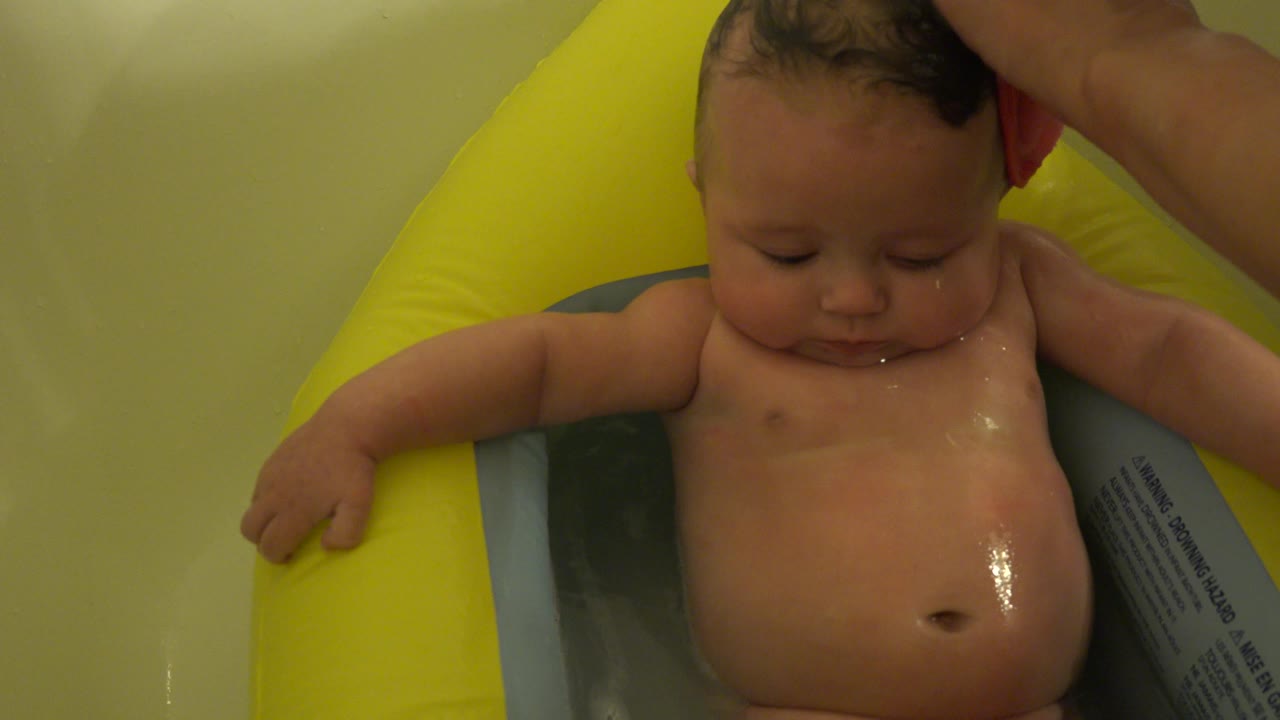 Baby in yellow bath support with water on the face and chest.