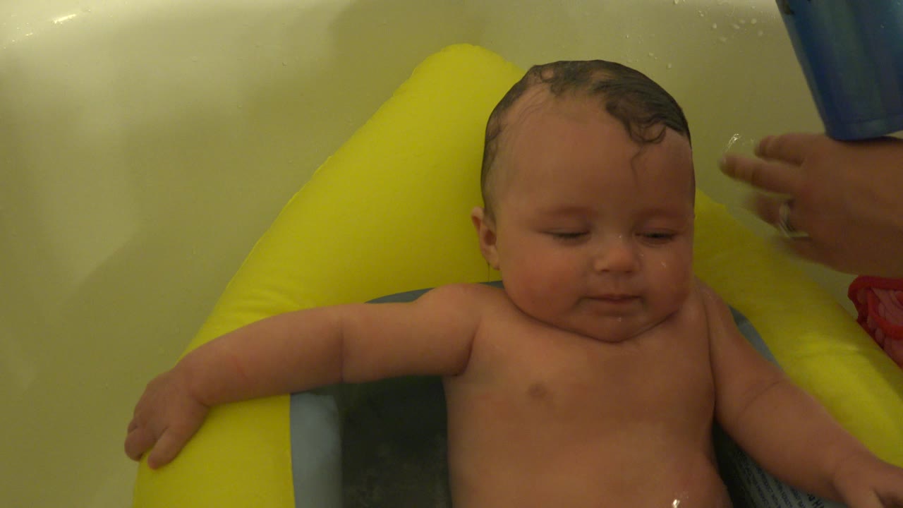 At the start of the Westminster, Colorado clip, a baby faces the camera while seated in a bright inflatable bath support in a bathtub.