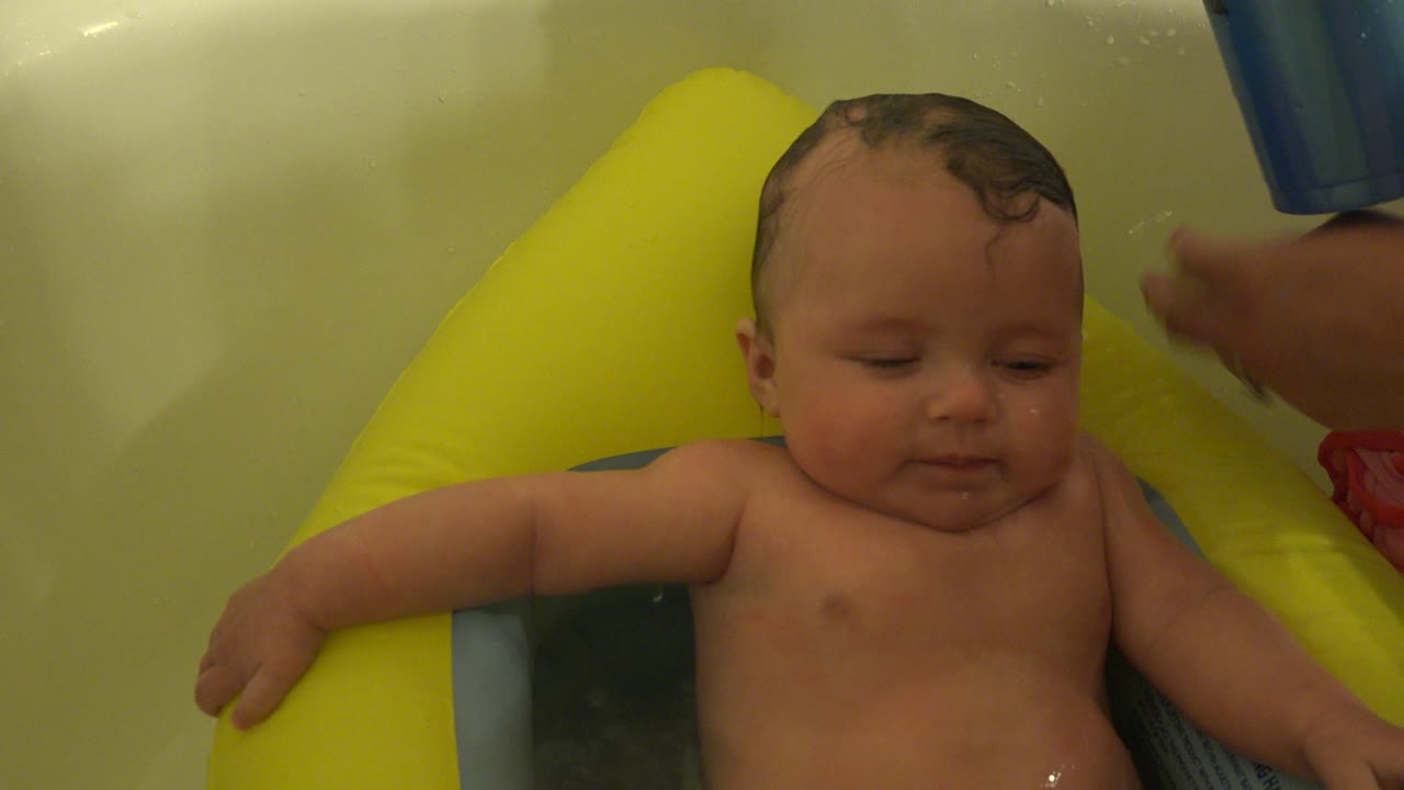 One second in, the baby remains centered in the Westminster, Colorado bathtub as an adult hand moves near the child's head and shoulder.