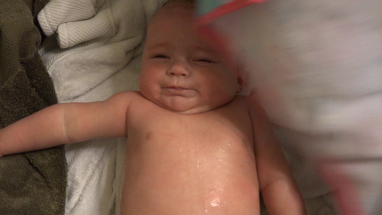 Wet baby lying on towels with a towel blurred in the foreground.