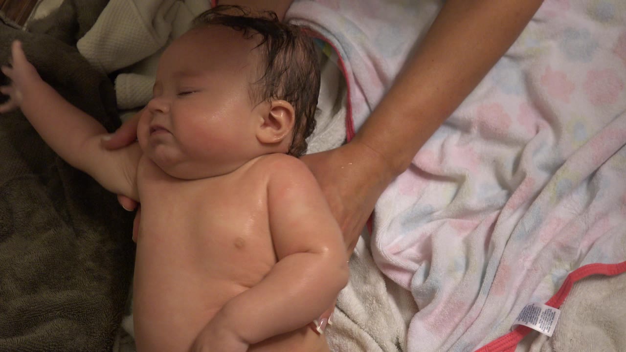Baby lying on towels while an adult arm rests nearby.