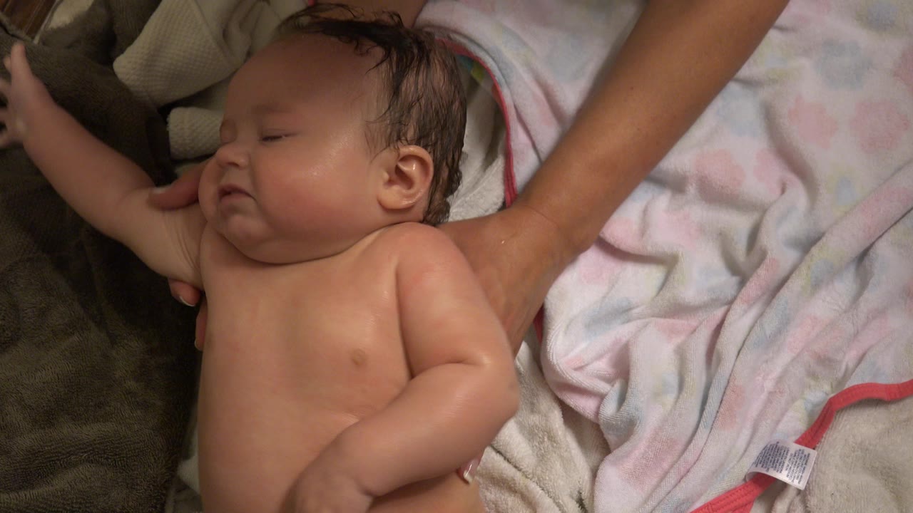 Baby girl on towels in Westminster, Colorado, with one arm extended and an adult arm visible near the top of the frame.