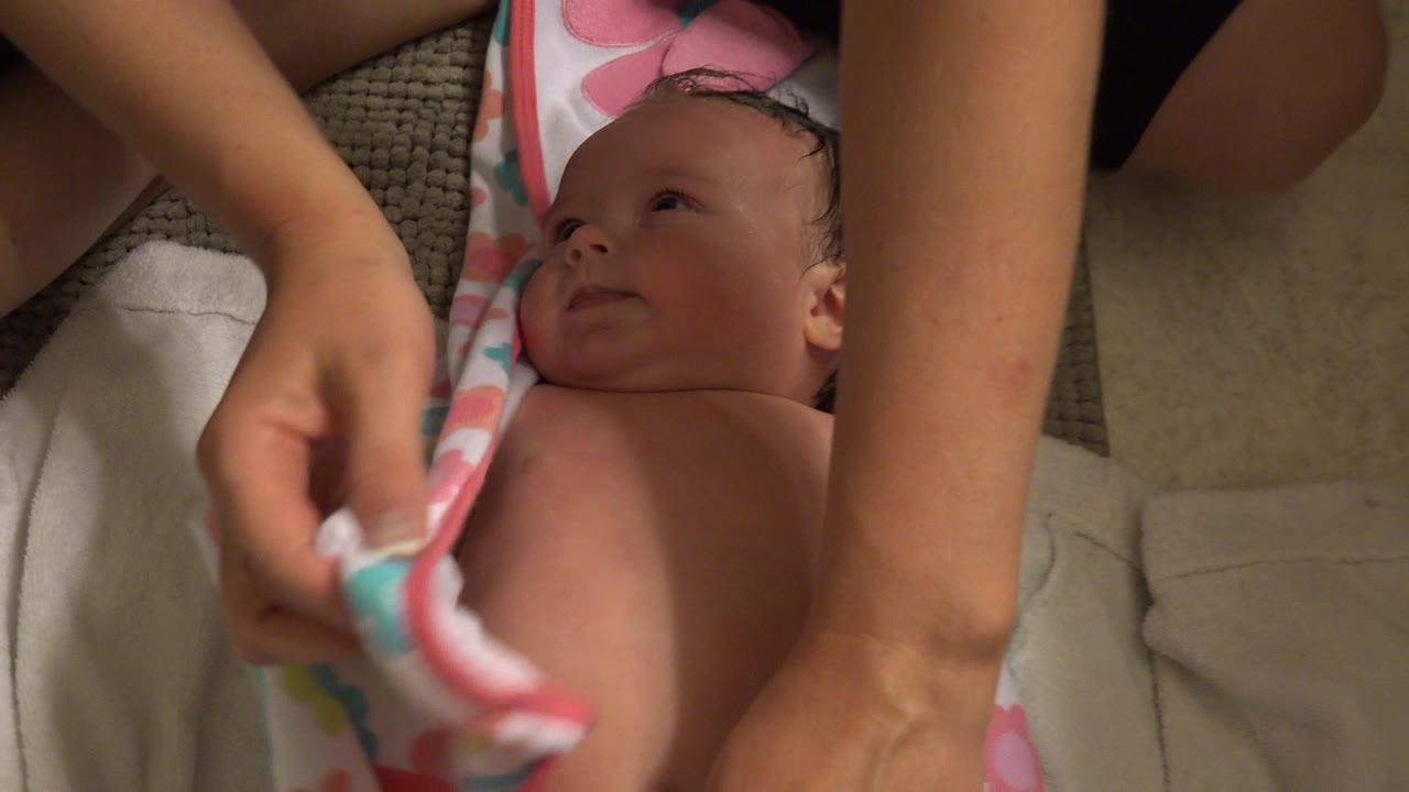 Baby lying on towels while adult hands pull a patterned bath towel nearby.