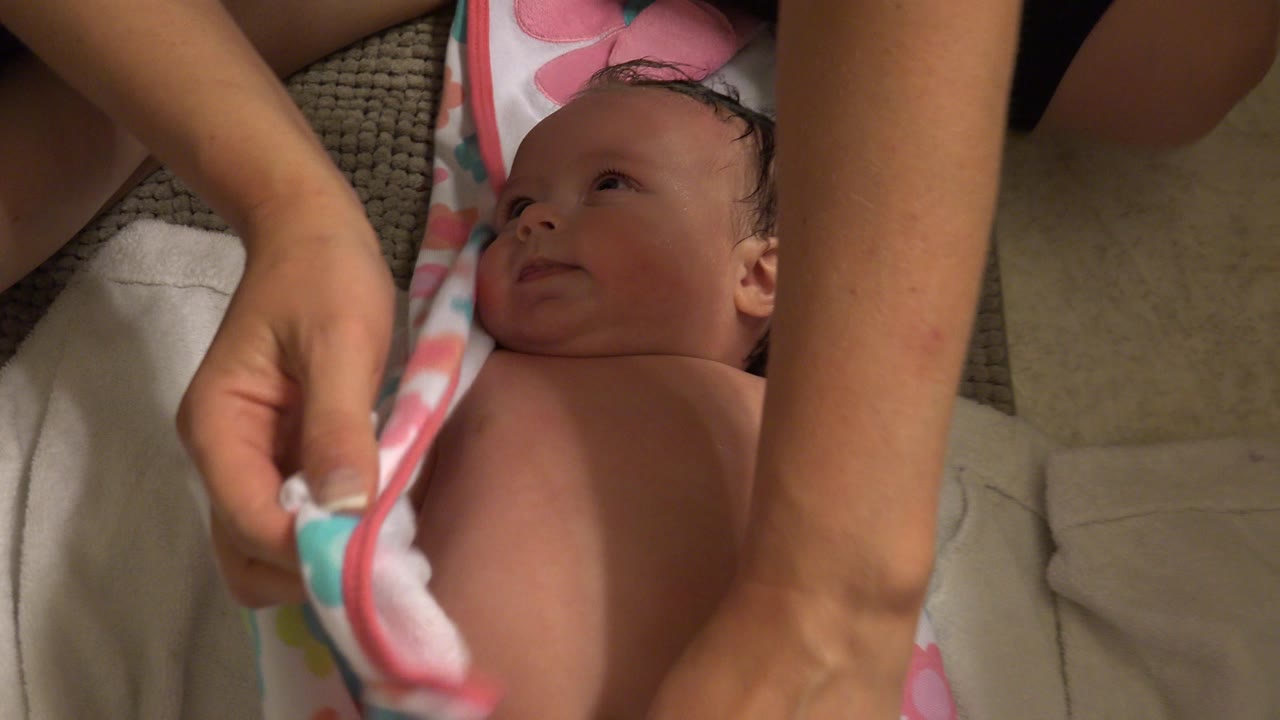 The baby remains on the towels while adult hands hold the patterned towel at the side of the frame in the Westminster, Colorado home setting.