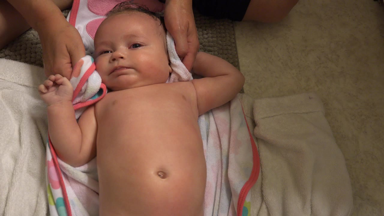 Baby lying on towels while an adult hand wipes near the head.