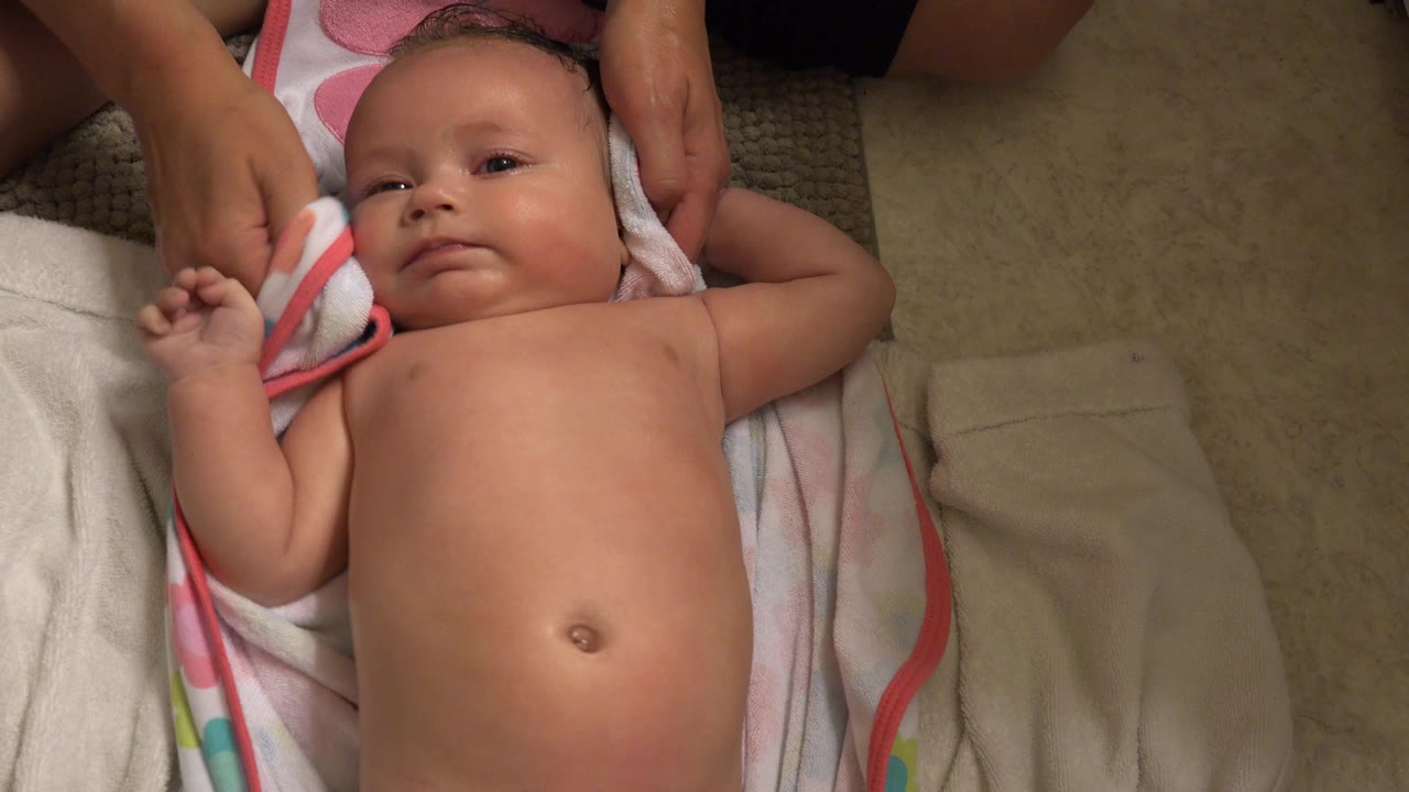 In Westminster, Colorado, the baby looks upward while an adult hand holds a striped towel along the side of the baby's head on the bathroom floor.