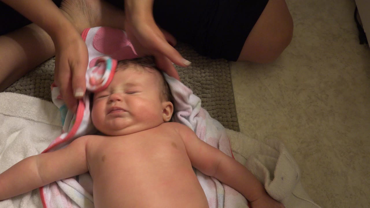 Adult hands dry a baby's wet hair with a pink-trimmed towel.