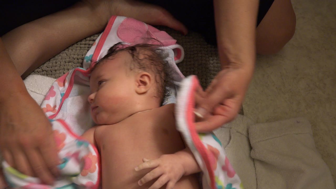 In Westminster, Colorado, adult hands pull a soft towel near a baby resting on layered bath towels on the floor.