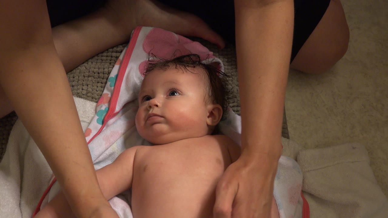 Adult arm crosses above a baby lying on a towel.