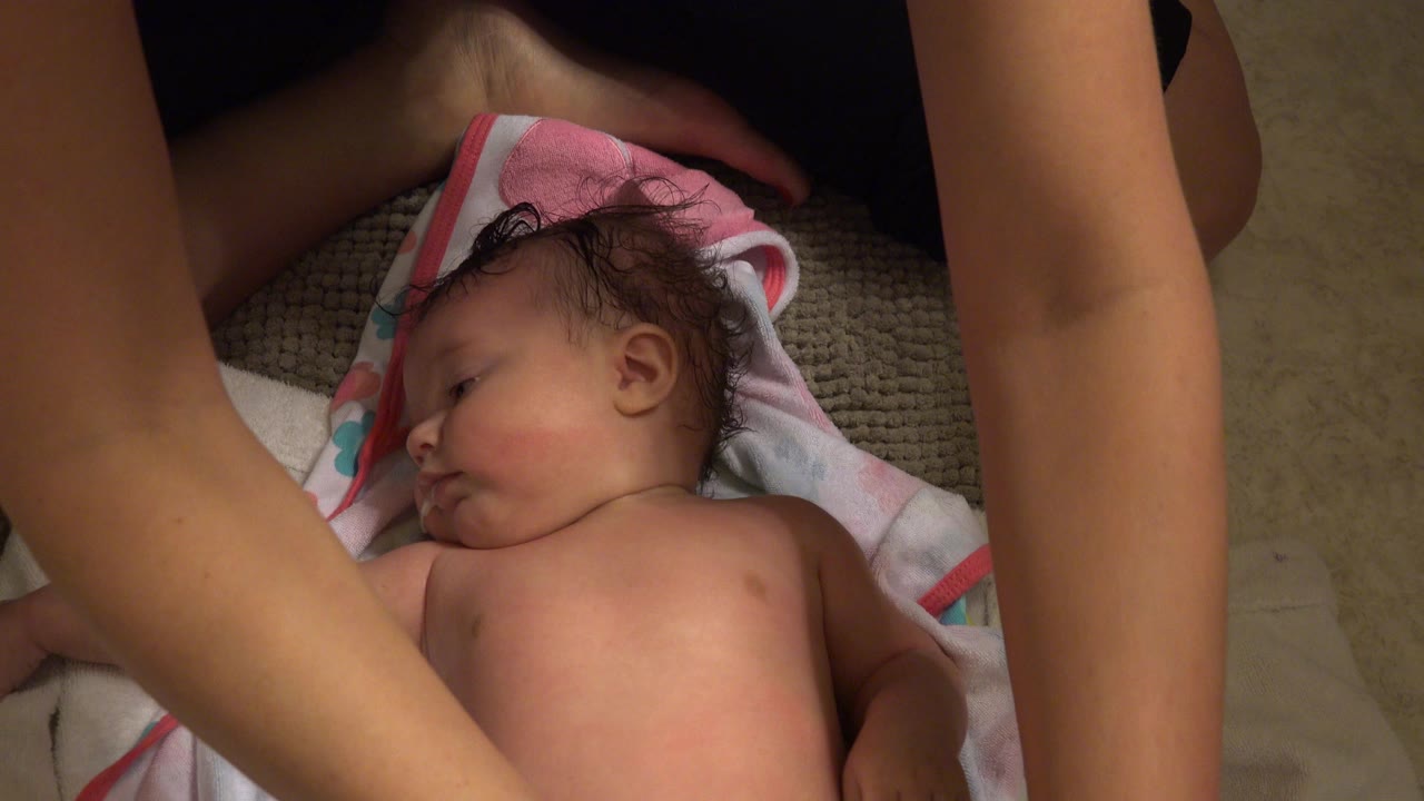 Infant lying on towels while adult arms reach in.