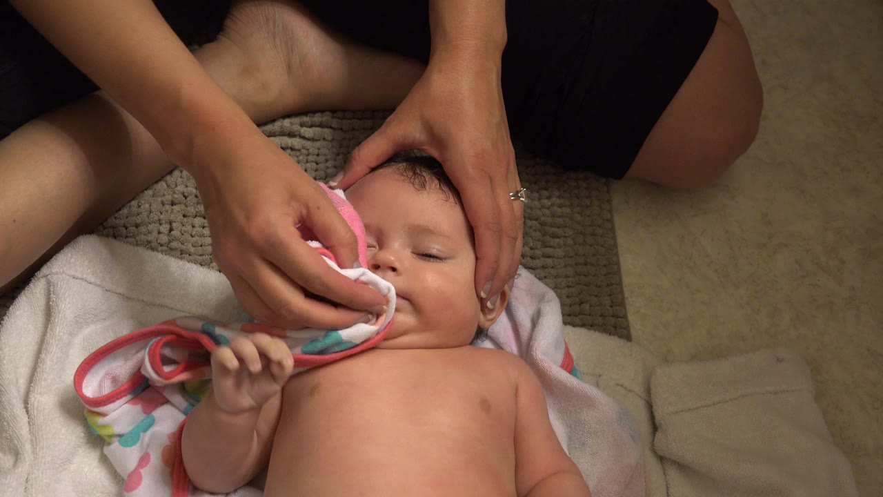 Woman's hands wipe a baby's face with a pink towel.
