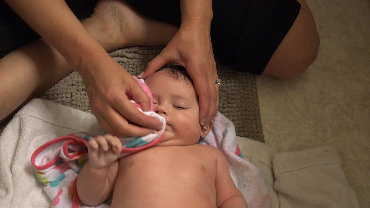 In Westminster, Colorado, the baby remains centered on the blanket while the caregiver presses the pink towel along the infant's cheek and mouth area.