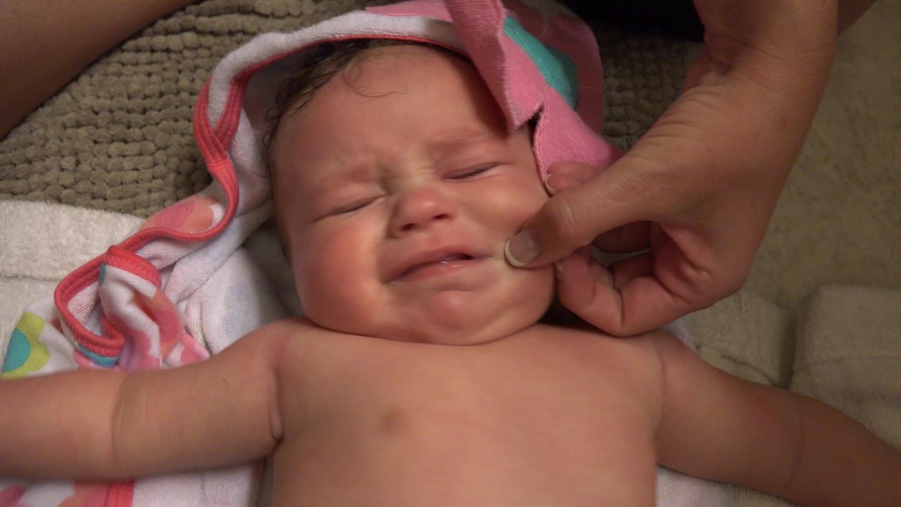 Crying baby on a towel while an adult hand touches the cheek.