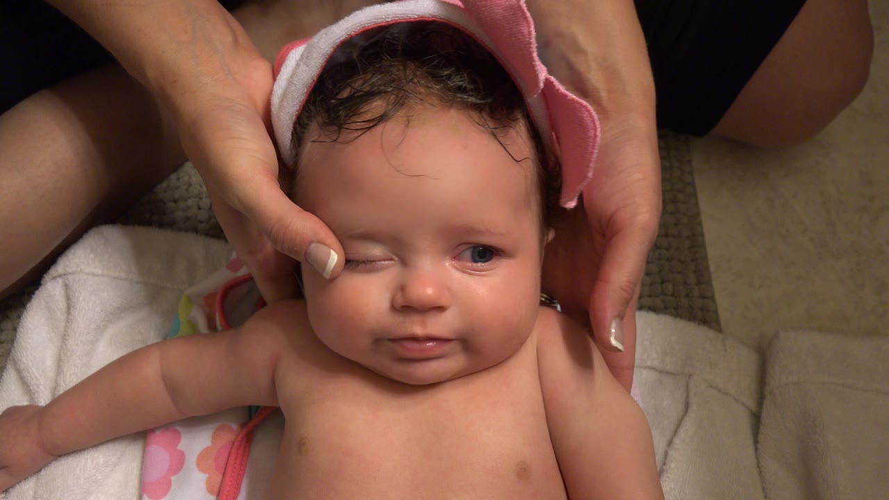 In Westminster, Colorado, the baby looks slightly to one side as adult hands keep the pink bath towel positioned around the head on the bathroom floor.
