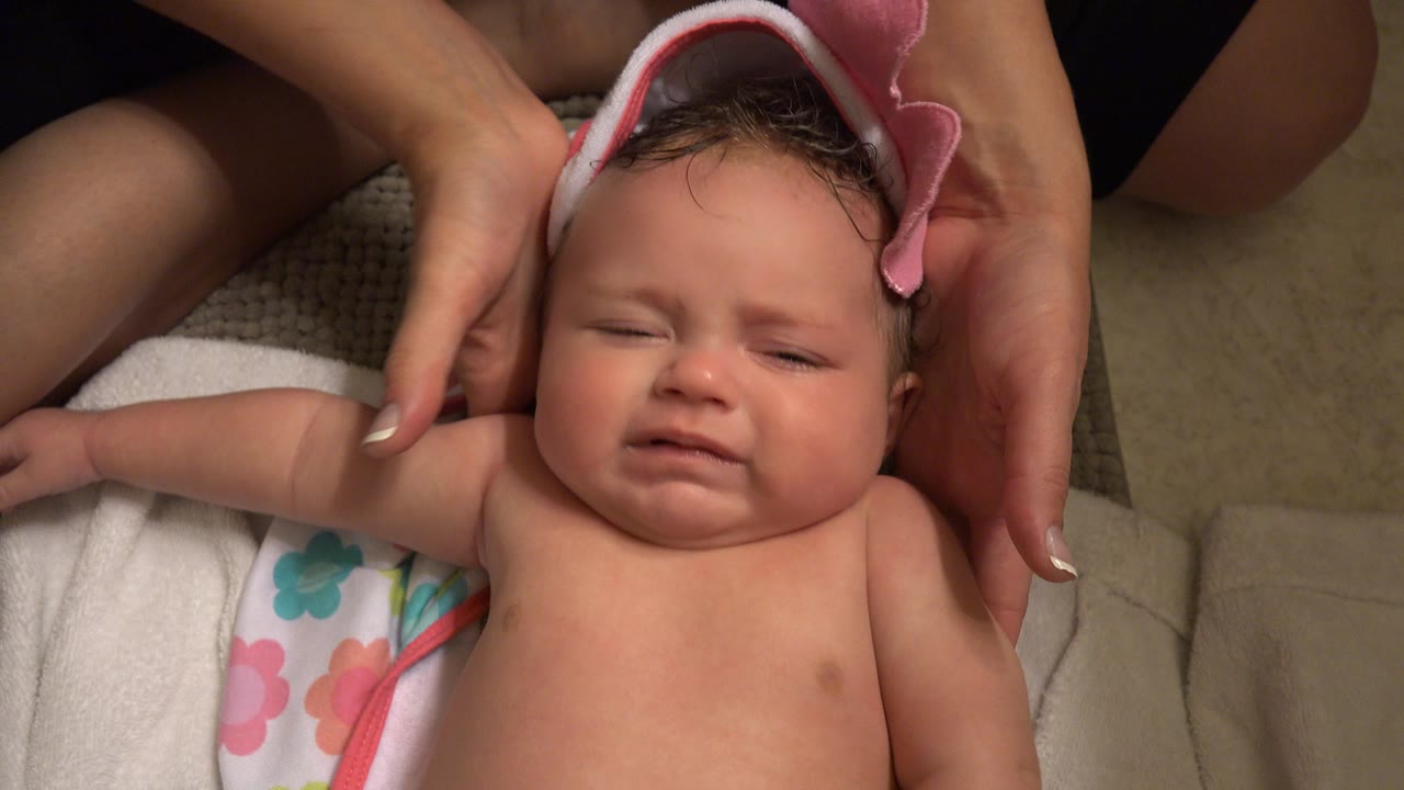 Baby beginning to cry as adult hands hold the towel near the ears.