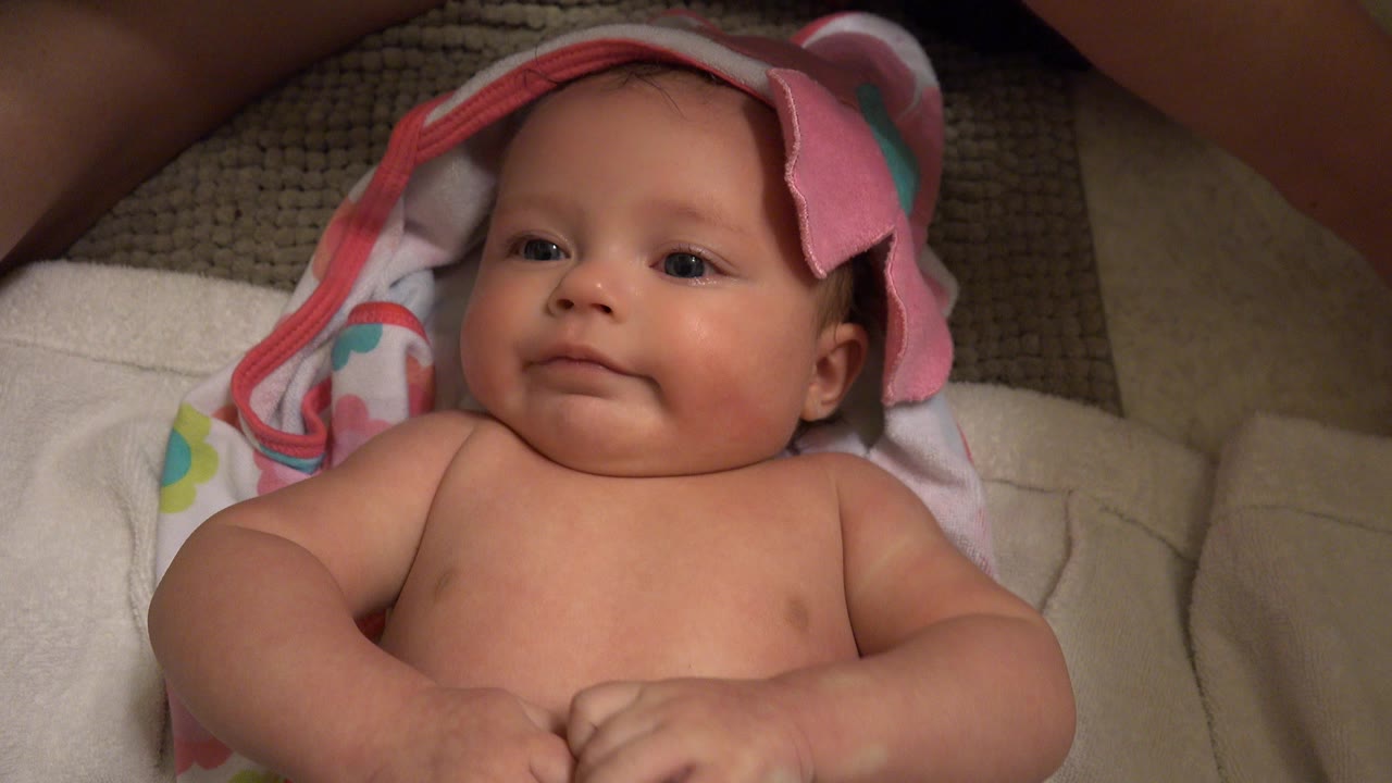 Infant lying on a towel with a pink hooded towel behind the head.